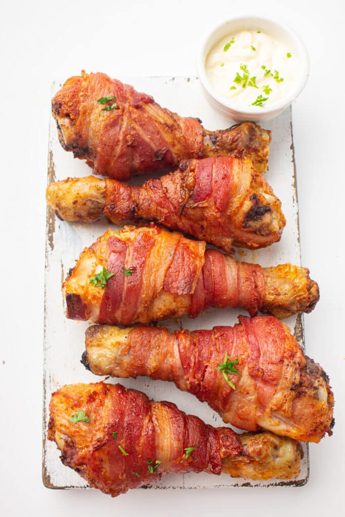 A picture of cooked bacon-wrapped chicken drumsticks with onion dip