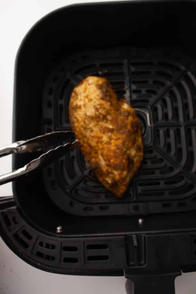 Air fryer chicken breast about to be flipped by tongs 